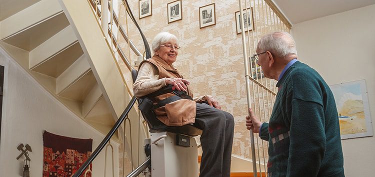 Elderly woman in a stairlift being watched by elderly man