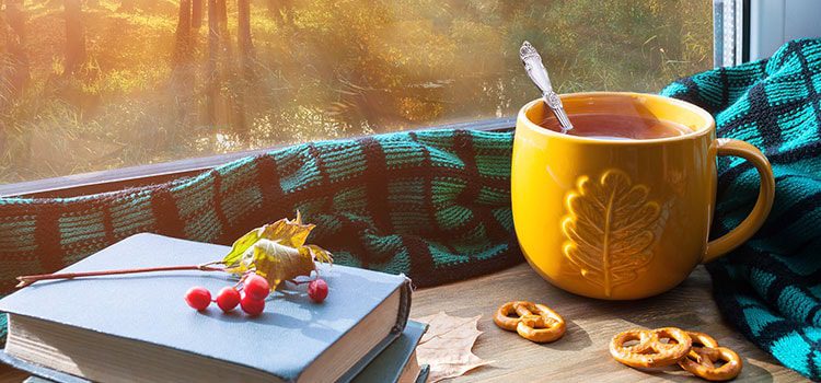 Close up of hot drink in a yellow mug surrounded by a blanket and a book