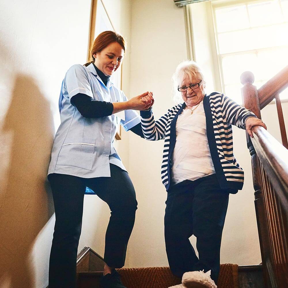 Caregiver assisting elderly woman down stairs