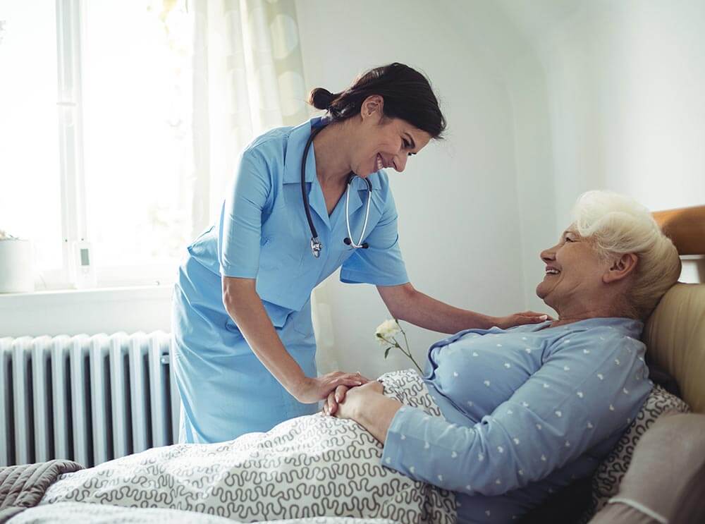 Caregiver comforting elderly woman in bed