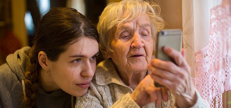 Young woman helping elderly woman use smartphone