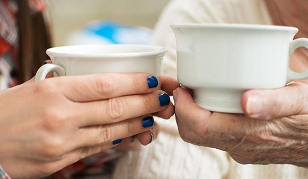 Elderly hand and younger hand holding mugs