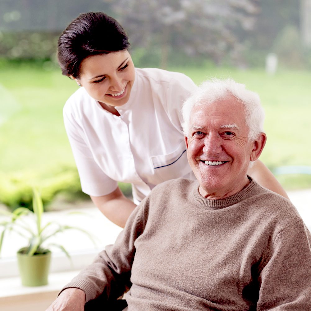 Caregiver smiling and standing behind elderly man