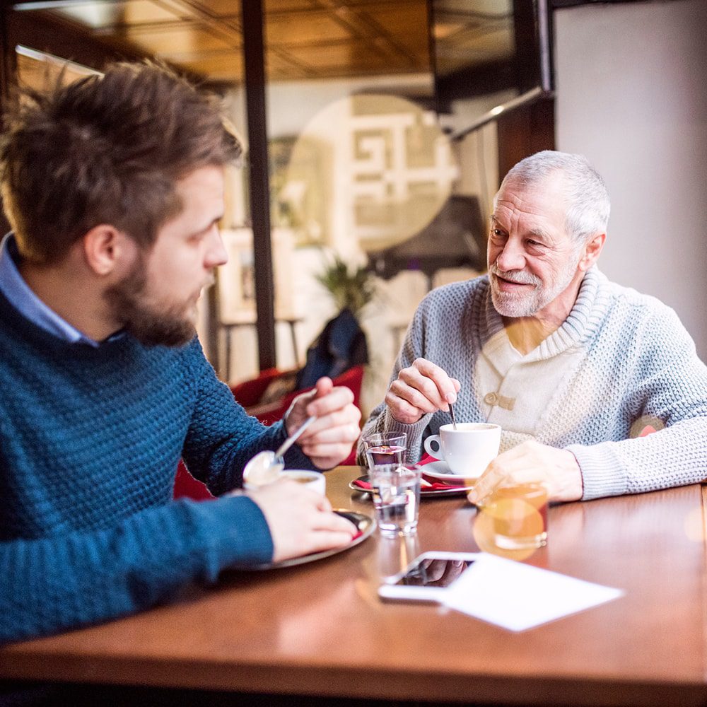 Young man having a conversation with elderly man in café