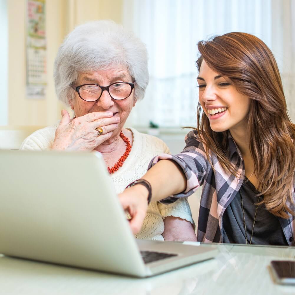 An elderly woman and a younger woman laughing at a laptop