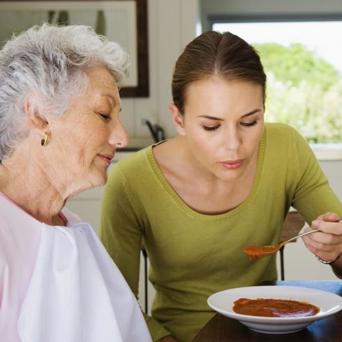 Woman feeding elderly woman soup