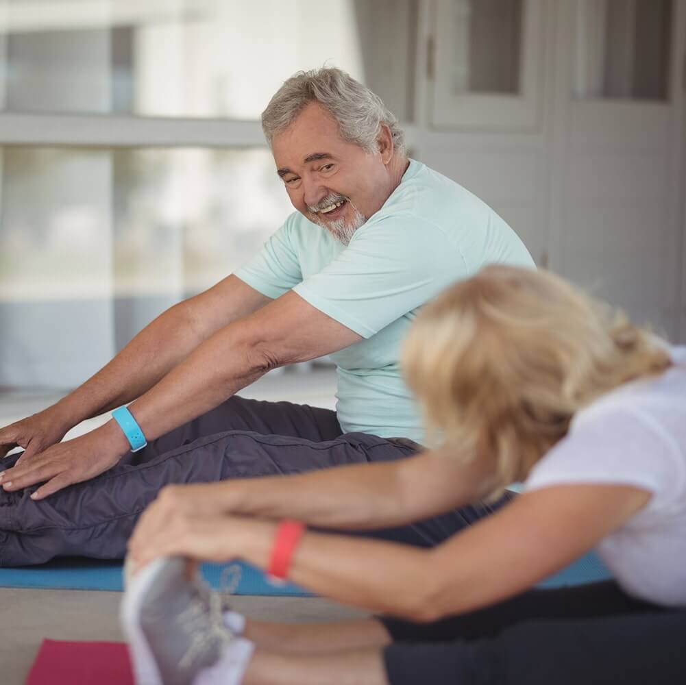 Woman and elderly man doing stretches on yoga mat