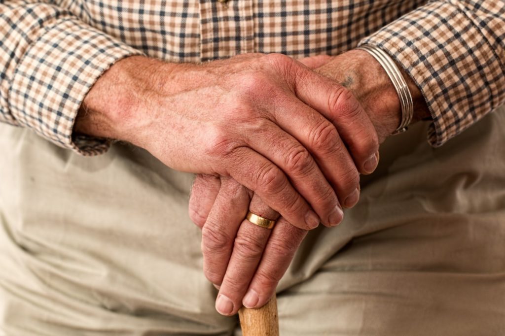 Close up of elderly man’s hands crossed holding a walking stick