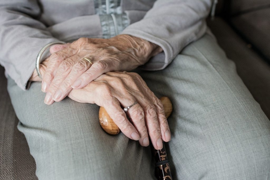 pair of elderly hands resting on a walking stick